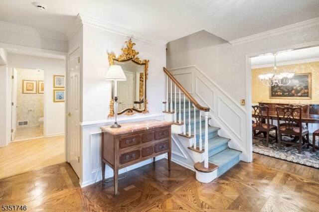 stairway with crown molding, a wainscoted wall, visible vents, and a notable chandelier