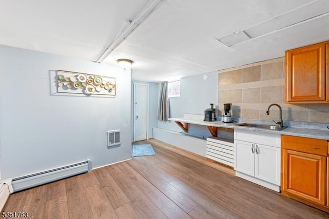 kitchen featuring wood finished floors, light countertops, a sink, and a baseboard radiator