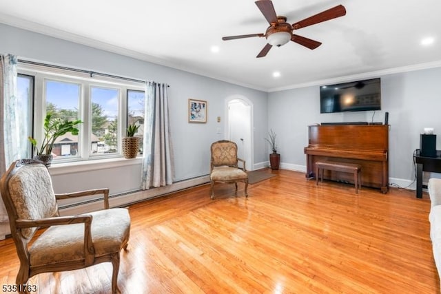 sitting room featuring crown molding, arched walkways, a baseboard radiator, and a ceiling fan