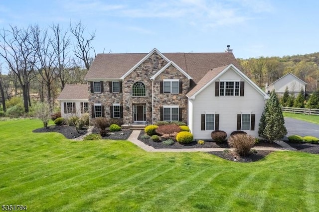 view of front of house with fence, a chimney, a front yard, and stone siding
