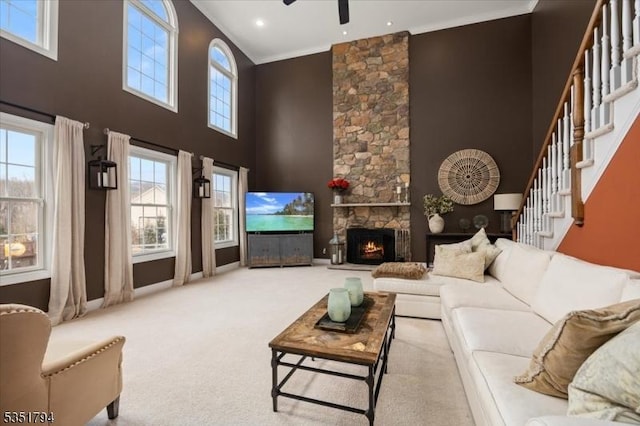 carpeted living area with ornamental molding, ceiling fan, a fireplace, stairway, and a high ceiling