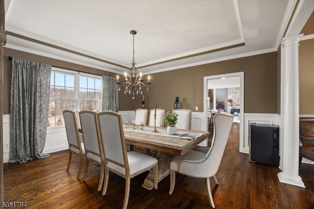 dining space featuring a decorative wall, ornamental molding, dark wood-style flooring, ornate columns, and a tray ceiling