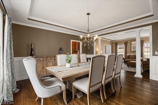 dining room featuring dark wood-style floors, ornate columns, a wainscoted wall, and a tray ceiling