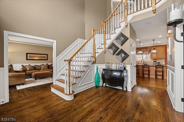 staircase featuring a decorative wall, a towering ceiling, a wainscoted wall, and wood finished floors