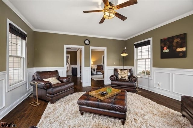 living area with a healthy amount of sunlight, a ceiling fan, a wainscoted wall, and dark wood finished floors