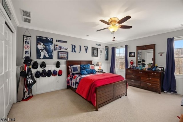 bedroom featuring visible vents, light carpet, multiple windows, and wainscoting