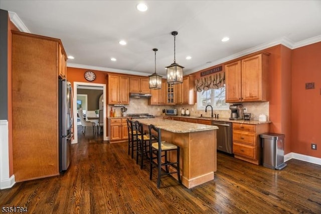 kitchen with appliances with stainless steel finishes, a kitchen island, brown cabinets, a kitchen bar, and a sink
