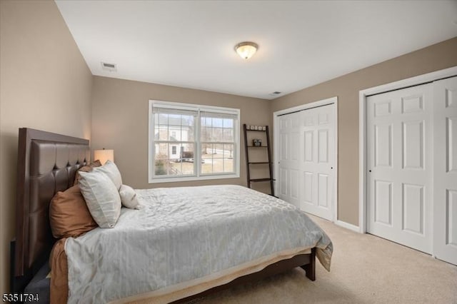 bedroom with baseboards, visible vents, light carpet, and multiple closets