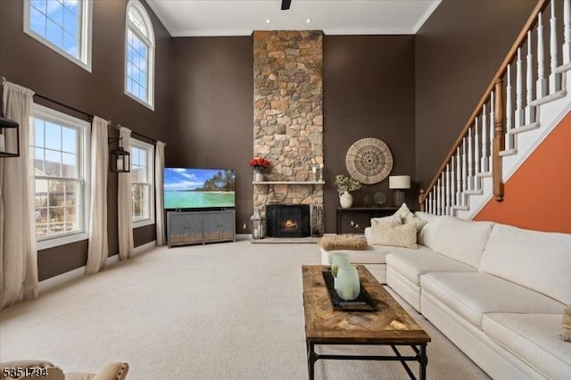 living area featuring a high ceiling, carpet flooring, stairs, a stone fireplace, and baseboards
