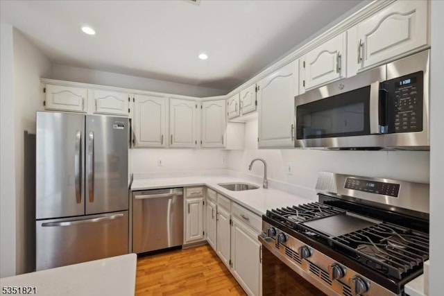 kitchen featuring recessed lighting, light countertops, a sink, light wood-type flooring, and appliances with stainless steel finishes
