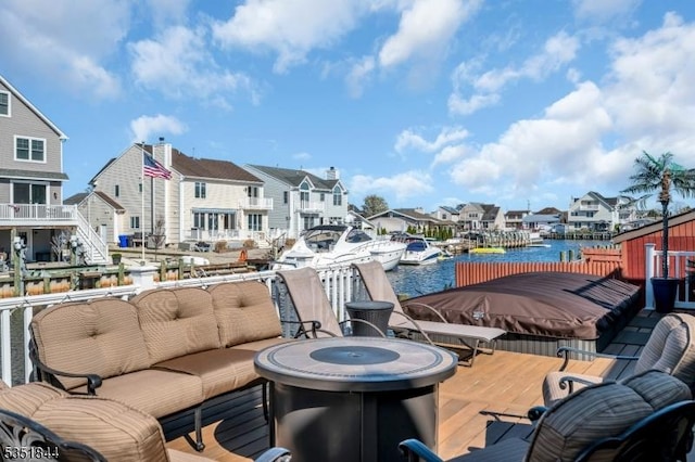 wooden terrace featuring a water view, an outdoor living space with a fire pit, and a residential view