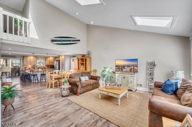 living room with a skylight, high vaulted ceiling, light wood finished floors, and visible vents