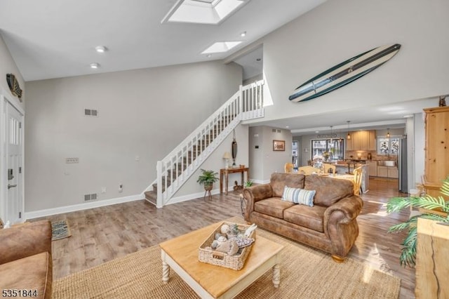 living room featuring visible vents, a high ceiling, stairway, light wood finished floors, and a skylight
