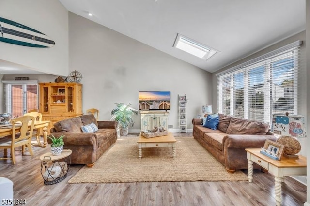 living area with baseboards, a skylight, wood finished floors, and high vaulted ceiling