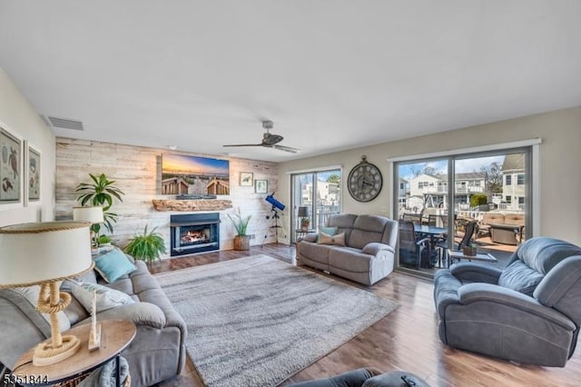 living area with visible vents, wood walls, wood finished floors, ceiling fan, and a lit fireplace