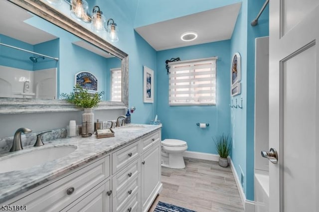 bathroom with double vanity, toilet, baseboards, and a sink