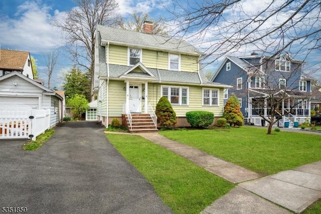 view of front facade with a chimney, a front lawn, an outdoor structure, a detached garage, and roof with shingles