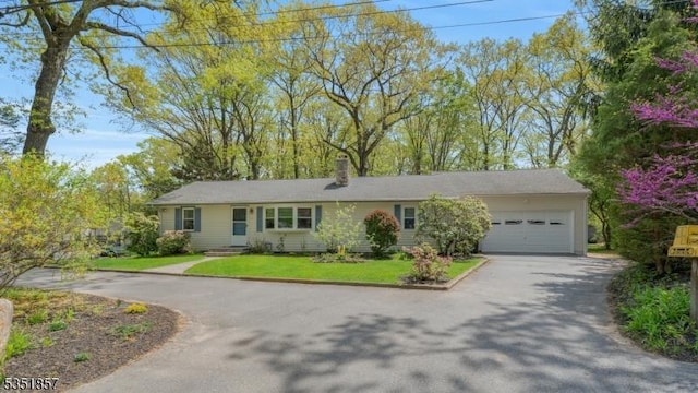 ranch-style home with an attached garage, a chimney, a front yard, and aphalt driveway