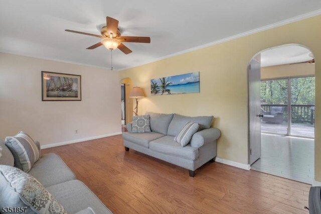 living area with baseboards, arched walkways, a ceiling fan, and wood finished floors