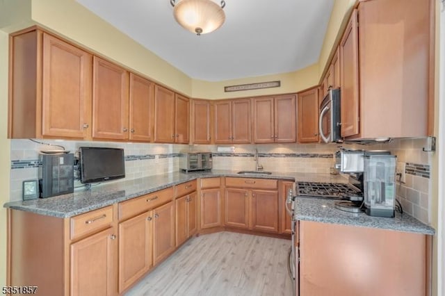 kitchen with light stone counters, a sink, backsplash, and stainless steel appliances