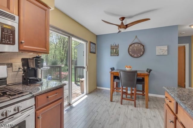 kitchen with a ceiling fan, light wood-type flooring, gas stove, baseboards, and dark stone counters