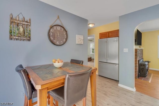 dining room with light wood-type flooring, a wood stove, baseboards, and arched walkways