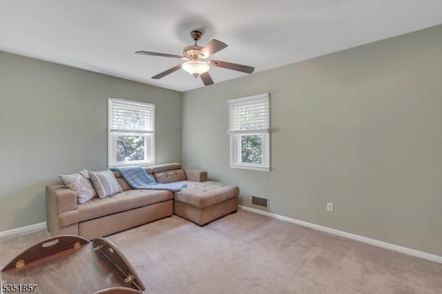 living area with baseboards, visible vents, a ceiling fan, and light colored carpet