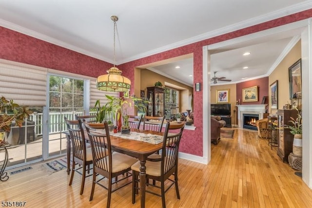 dining room featuring visible vents, baseboards, ceiling fan, a warm lit fireplace, and light wood-style flooring