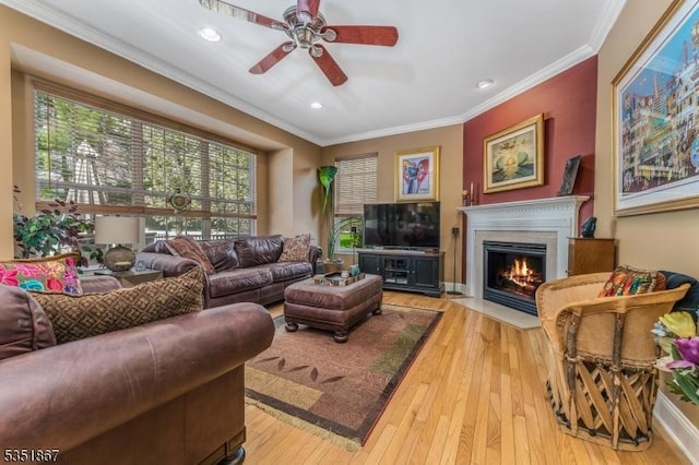 living area with crown molding, light wood-style floors, a ceiling fan, recessed lighting, and a fireplace with flush hearth