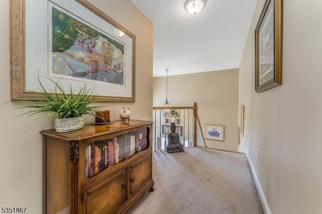 hallway with baseboards, carpet flooring, and an upstairs landing