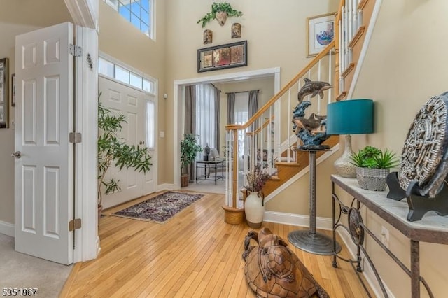 foyer featuring wood-type flooring, baseboards, a high ceiling, and stairway