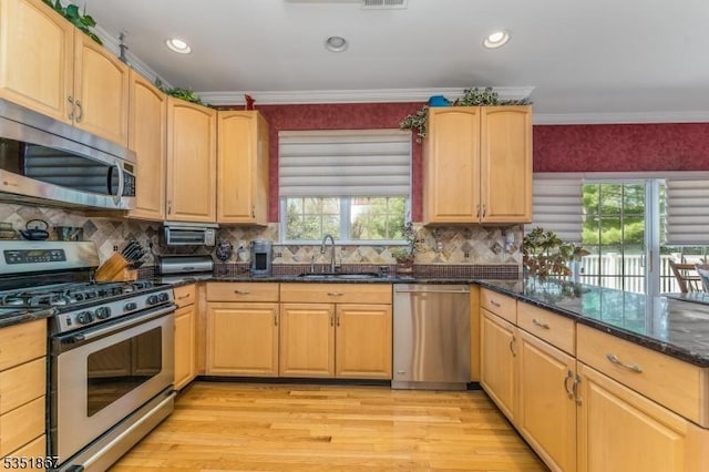 kitchen with light wood-type flooring, a sink, dark stone counters, and appliances with stainless steel finishes