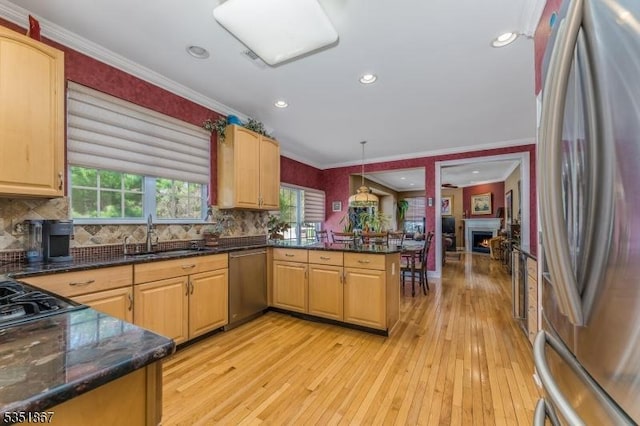 kitchen featuring appliances with stainless steel finishes, a sink, light wood-type flooring, backsplash, and ornamental molding