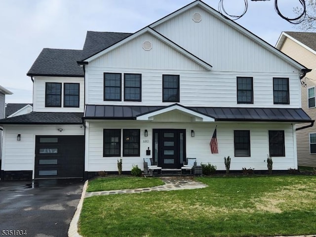 modern inspired farmhouse with a front lawn, aphalt driveway, a standing seam roof, a shingled roof, and an attached garage