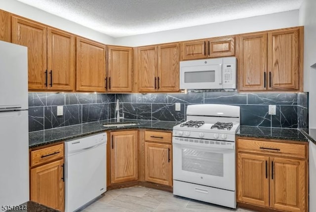 kitchen featuring tasteful backsplash, dark stone countertops, a sink, brown cabinets, and white appliances