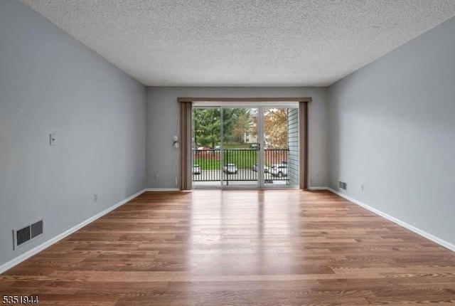 unfurnished room featuring baseboards, wood finished floors, visible vents, and a textured ceiling