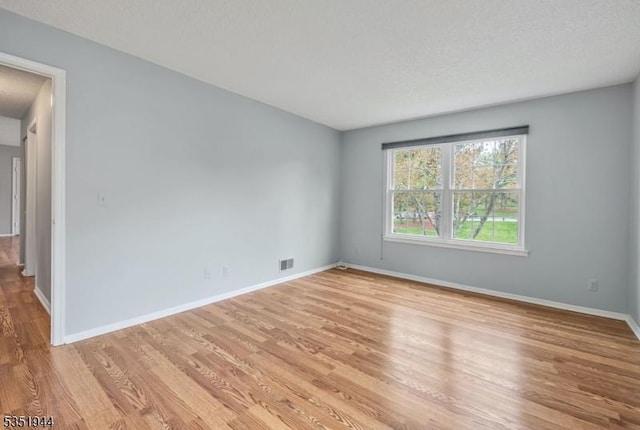 unfurnished room featuring light wood-style floors, visible vents, and baseboards