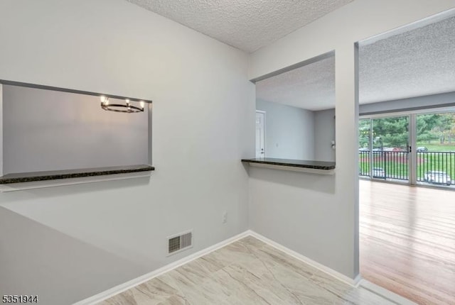 empty room featuring a textured ceiling, a chandelier, marble finish floor, baseboards, and visible vents