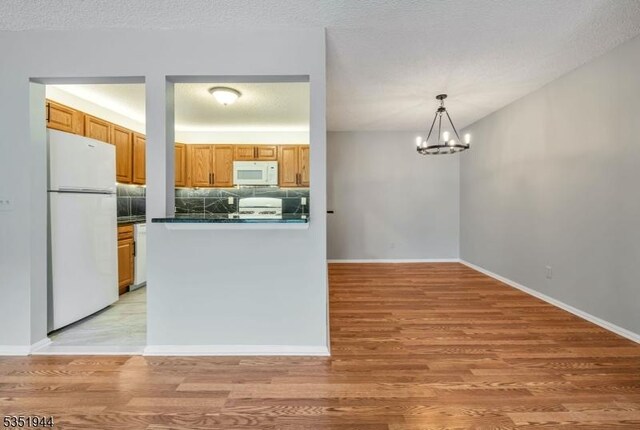 kitchen featuring dark countertops, a notable chandelier, light wood finished floors, and white appliances