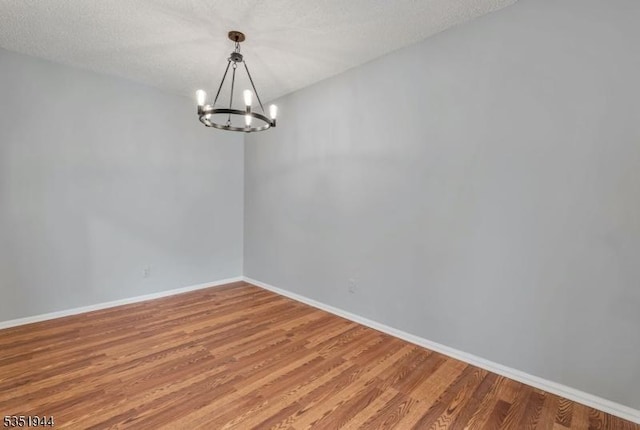 empty room featuring baseboards, a notable chandelier, a textured ceiling, and light wood-style flooring