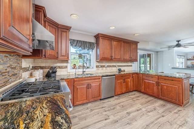 kitchen with appliances with stainless steel finishes, a sink, wall chimney exhaust hood, a peninsula, and stone counters
