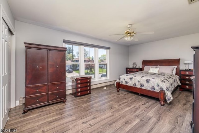 bedroom with ceiling fan, baseboard heating, baseboards, light wood-type flooring, and a closet