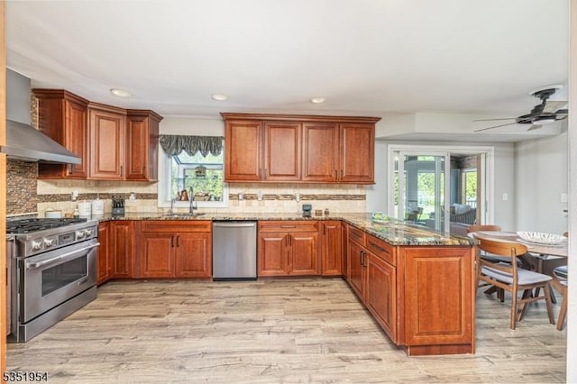 kitchen featuring wall chimney range hood, a peninsula, appliances with stainless steel finishes, and plenty of natural light