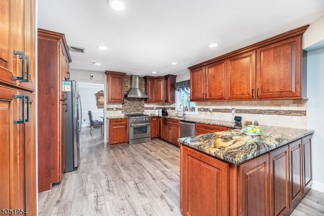 kitchen with wall chimney range hood, appliances with stainless steel finishes, light wood-style floors, a peninsula, and visible vents