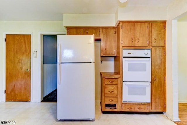 kitchen featuring light floors, baseboards, brown cabinetry, and white appliances