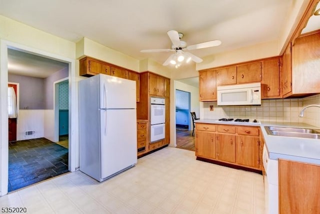 kitchen with white appliances, ceiling fan, light countertops, a wainscoted wall, and a sink