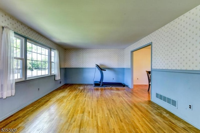 unfurnished living room with visible vents, baseboards, wood finished floors, and wallpapered walls