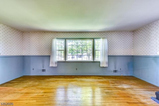 spare room with wallpapered walls, wood finished floors, and visible vents