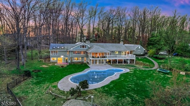 back of property at dusk with stairs, an outdoor pool, a yard, a patio area, and a deck
