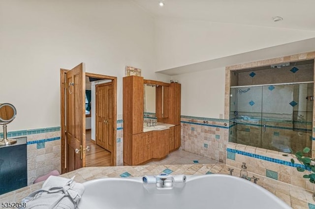 full bathroom featuring a shower stall, a tub, a wainscoted wall, and tile walls